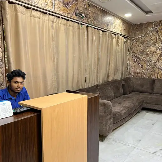 The clinic's reception counter with a computer and a QR-code payment speaker on it and a member of staff seated behind it, floor-length beige curtains along one wall and a brown corner sofa against polished brown marble.